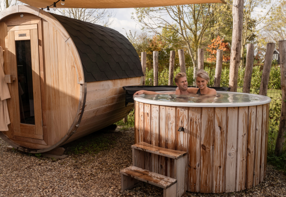 Koppel ontspant in een hottub en sauna buiten bij Water lodge 6 Deluxe, omgeven door houten hek.