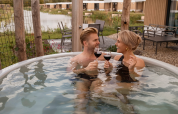 Paar genießt ein Glas Wein im Whirlpool der Water lodge 6 Deluxe mit Sauna im Hofparken Wiltershaar.