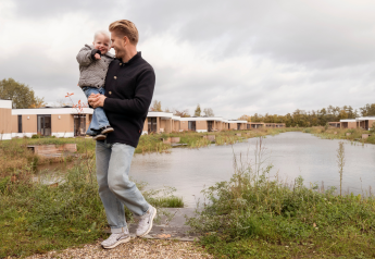 Homme avec enfant près du lac à Water lodge 6 Deluxe à Hofparken Wiltershaar, Pays-Bas, temps nuageux.