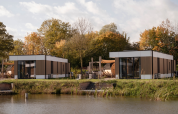 Modern water lodge by a lake at Hofparken Wiltershaar in the Netherlands, surrounded by autumn trees.