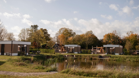 Vue du Water lodge 6 Deluxe avec sauna et jacuzzi au Hofparken Wiltershaar, Pays-Bas, au bord d’un étang.