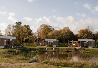 Vue du Water lodge 6 Deluxe avec sauna et jacuzzi au Hofparken Wiltershaar, Pays-Bas, au bord d’un étang.