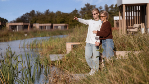 To personer ved søen foran Water lodge 6 Deluxe på Hofparken Wiltershaar, afslappende omgivelser.