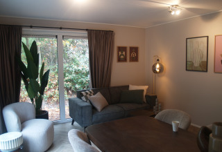 Moderne leefruimte met grijze zetel, fauteuil, groot raam en decoratie in Groeneborg lodge, Nederland.