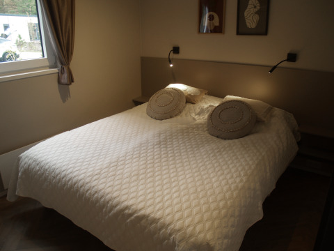 Gezellige lodge slaapkamer met een dubbel bed, witte gespikkelde sprei en ronde kussens op het bed.