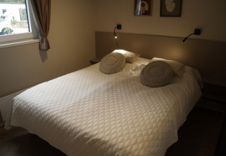 Gezellige lodge slaapkamer met een dubbel bed, witte gespikkelde sprei en ronde kussens op het bed.