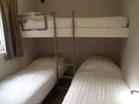 Habitación de una cabaña con dos camas individuales en el suelo y una litera superior con escalera.