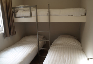 Een kamer in een lodge met twee enkele bedden beneden en een enkel bovenbed met ladder.