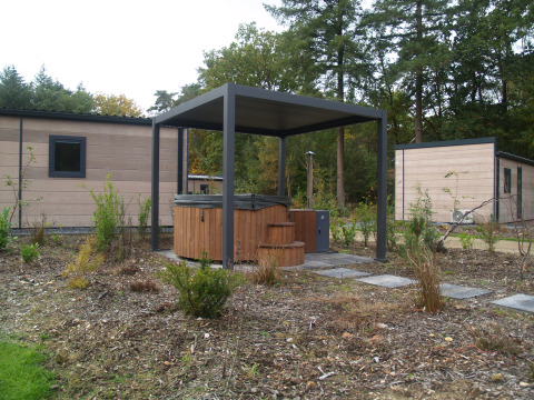 Outdoor hot tub with canopy in front of modern lodges surrounded by greenery at Groeneborg lodge.