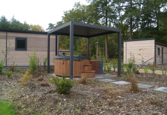 Udendørs boblebad med overdækning foran moderne hytter i grønne omgivelser på Groeneborg lodge.