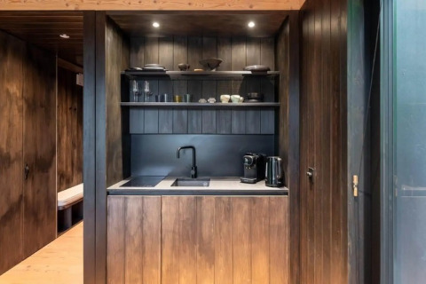 Moderne Küchenzeile in der Nokken Forest Cabin in Wilsumer Berge, Deutschland, mit dunklen Holzpaneelen.