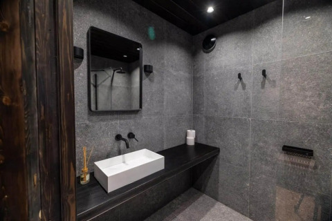 Baño moderno en Nokken Forest Cabin con azulejos grises, encimera negra y lavabo rectangular blanco.