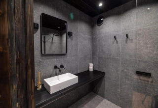Moderne badkamer in Nokken Forest Cabin met grijze tegels, zwart werkblad en witte wastafel in Duitsland.