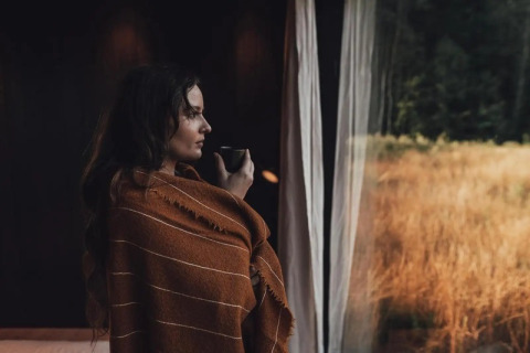 Vrouw met deken en tas kijkt uit het raam van Nokken Forest Cabin in Wilsumer Berge, Duitsland.