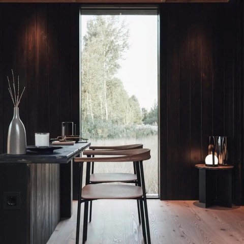 Modern interieur van Nokken Forest Cabin in Duitsland met donker hout, groot raam en uitzicht op natuur.
