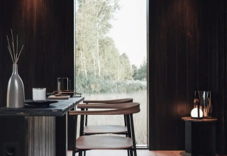 Interni moderni della Nokken Forest Cabin in Germania con legno scuro, ampia finestra e vista sulla natura.