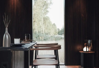 Interior moderno de la Nokken Forest Cabin en Alemania, madera oscura, ventana grande y vista a la naturaleza.