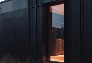Moderne schwarze Nokken Forest Cabin in Wilsumer Berge, Deutschland, mit offenem Fenster und hohem Gras.