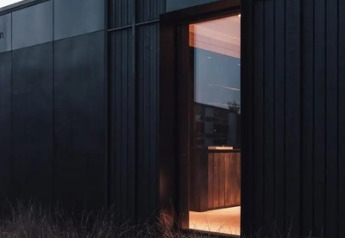 Modern black Nokken Forest Cabin exterior at Wilsumer Berge, Germany, with open window and wild grass.