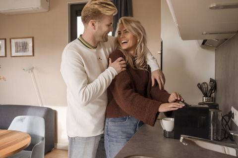 Young couple sharing a joyful moment in a cozy lodge kitchen as the woman prepares coffee for them.