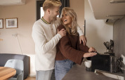 Young couple sharing a joyful moment in a cozy lodge kitchen as the woman prepares coffee for them.