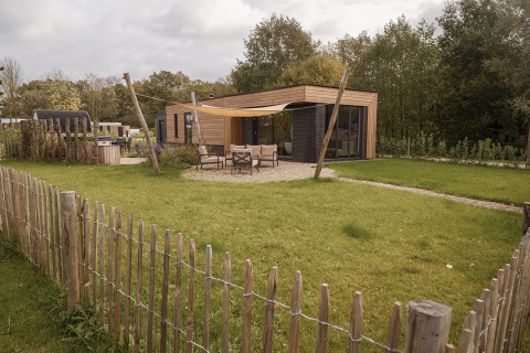 Photo d’un lodge moderne en bois avec terrasse, salon de jardin et espace clôturé dans un cadre verdoyant.