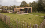 Photo d’un lodge moderne en bois avec terrasse, salon de jardin et espace clôturé dans un cadre verdoyant.