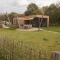 Foto van een moderne houten lodge met terras, tuinset en omheinde tuin in een groene omgeving.