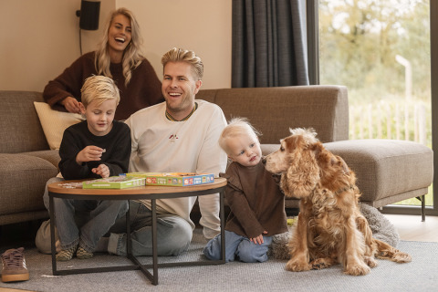 Family sits in a lodge living room, playing a board game with their kids and golden dog.