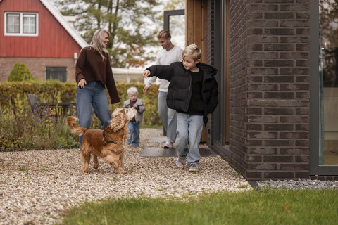 Famille profitant du plein air devant un lodge, enfants et chien jouent ensemble sur le chemin de gravier.