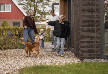 Family enjoying time outside a lodge, with children and a dog playing together on a gravel path.