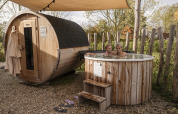 Een koppel ontspant in een houten hottub naast een tonvormige sauna bij een charmante lodge.