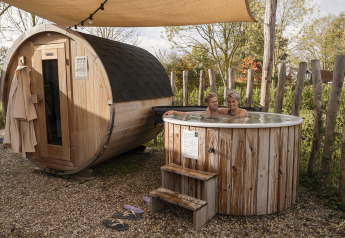 Una pareja se relaja en una bañera de hidromasaje al aire libre junto a una sauna de barril en una cabaña.