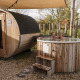 A couple relaxes in a wooden hot tub next to a barrel sauna at a cozy lodge surrounded by nature.