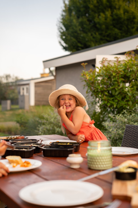 Una bambina felice con abito estivo e cappello si gode un pasto all'aperto a Schaelsbergerbosch, Paesi Bassi.