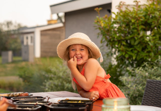 Una niña sonriente con vestido de verano y sombrero disfruta de una comida al aire libre en Schaelsbergerbosch, Países Bajos.
