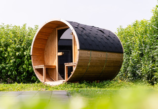 Ronde houten buitensauna met zitbank bij de ingang, omgeven door groen bij Resort Mooi Bemelen, Nederland.