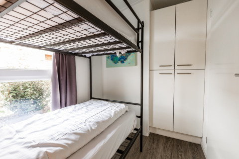 Moderne slaapkamer met stapelbed, groot raam, gordijnen en witte kasten in Schaelsbergerbosch Lodge.