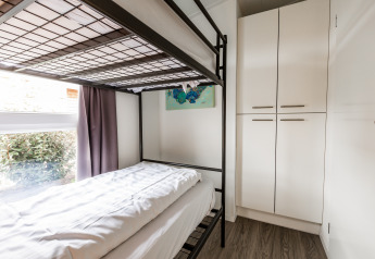 Dormitorio moderno con litera, ventana grande, cortinas y armarios blancos en Schaelsbergerbosch Lodge.