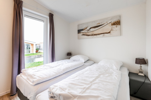 Lichte slaapkamer in Schaelsbergerbosch-lodge met twee eenpersoonsbedden en boot schilderij aan de muur.