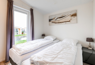 Lichte slaapkamer in Schaelsbergerbosch-lodge met twee eenpersoonsbedden en boot schilderij aan de muur.