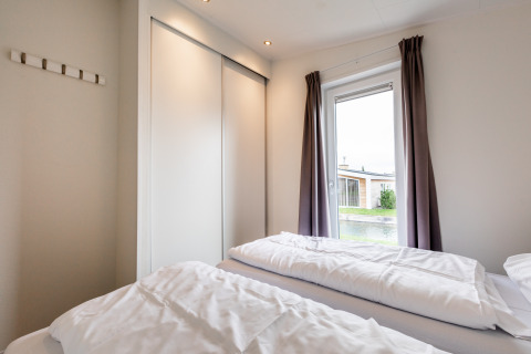 Lichte slaapkamer met twee eenpersoonsbedden, grote kasten en raam met gordijnen bij Resort Mooi Bemelen.