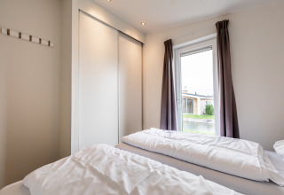 Lichte slaapkamer met twee eenpersoonsbedden, grote kasten en raam met gordijnen bij Resort Mooi Bemelen.