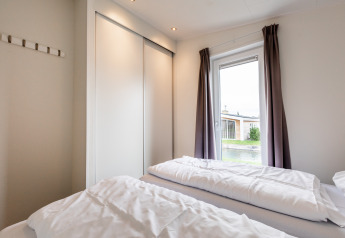 Chambre lumineuse avec deux lits simples, grande armoire et fenêtre avec rideaux au Resort Mooi Bemelen.