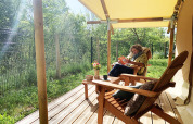 Persona che legge sulla terrazza di una tenda safari Bivouac Comfort al campeggio Le Val de Cesse in Francia.