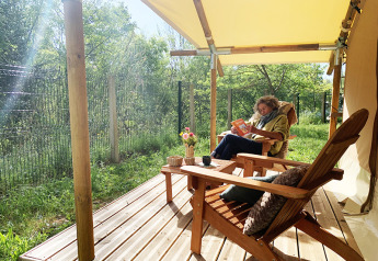 Persona che legge sulla terrazza di una tenda safari Bivouac Comfort al campeggio Le Val de Cesse in Francia.