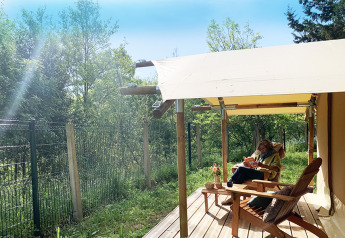 Mujer leyendo en la terraza de la tienda safari Bivouac Comfort en Camping Le Val de Cesse, Francia.