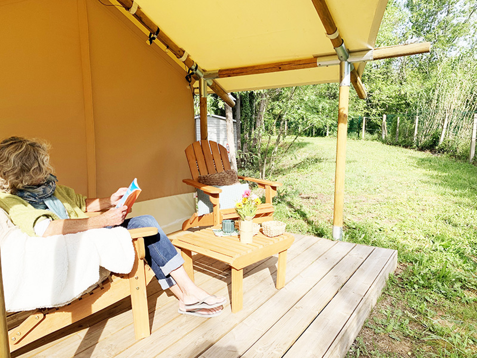 Vrouw leest op de veranda van een Bivouac Comfort safaritent op Camping Le Val de Cesse in Frankrijk.