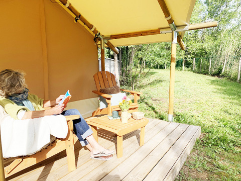 Vrouw leest op het terras van een Bivouac Comfort safaritent bij Camping Le Val de Cesse in Frankrijk.