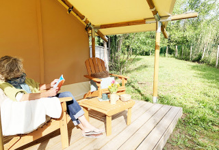 Vrouw leest op het terras van een Bivouac Comfort safaritent bij Camping Le Val de Cesse in Frankrijk.